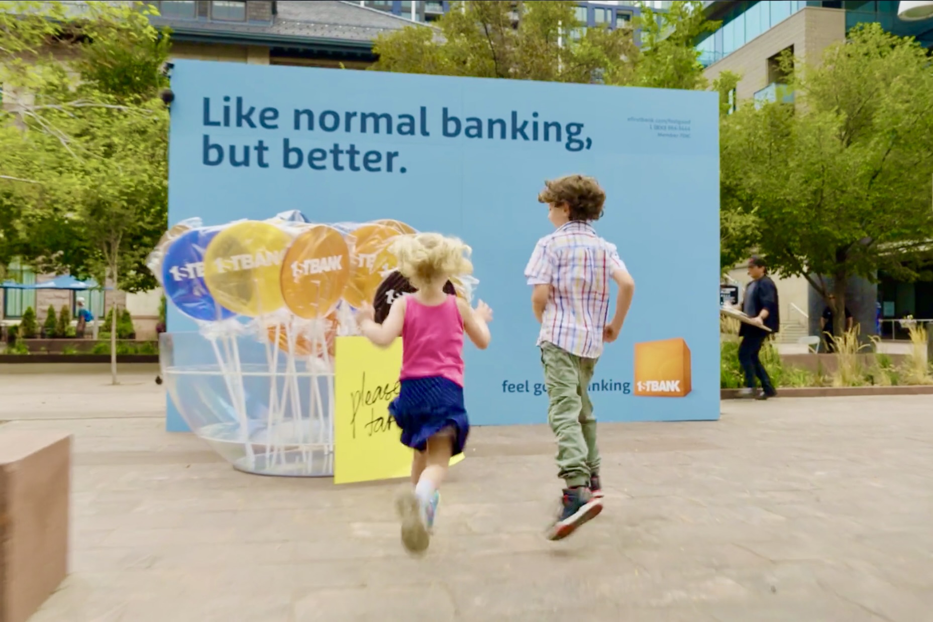 Children running toward oversized First Bank branded lollipops at an outdoor activation.