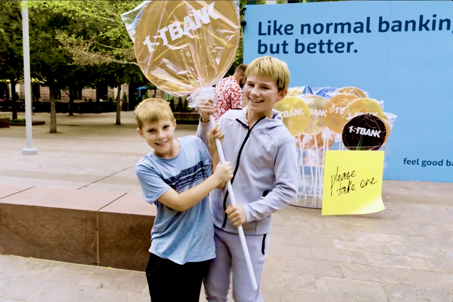 Two children holding an oversized yellow First Bank branded lollipop.